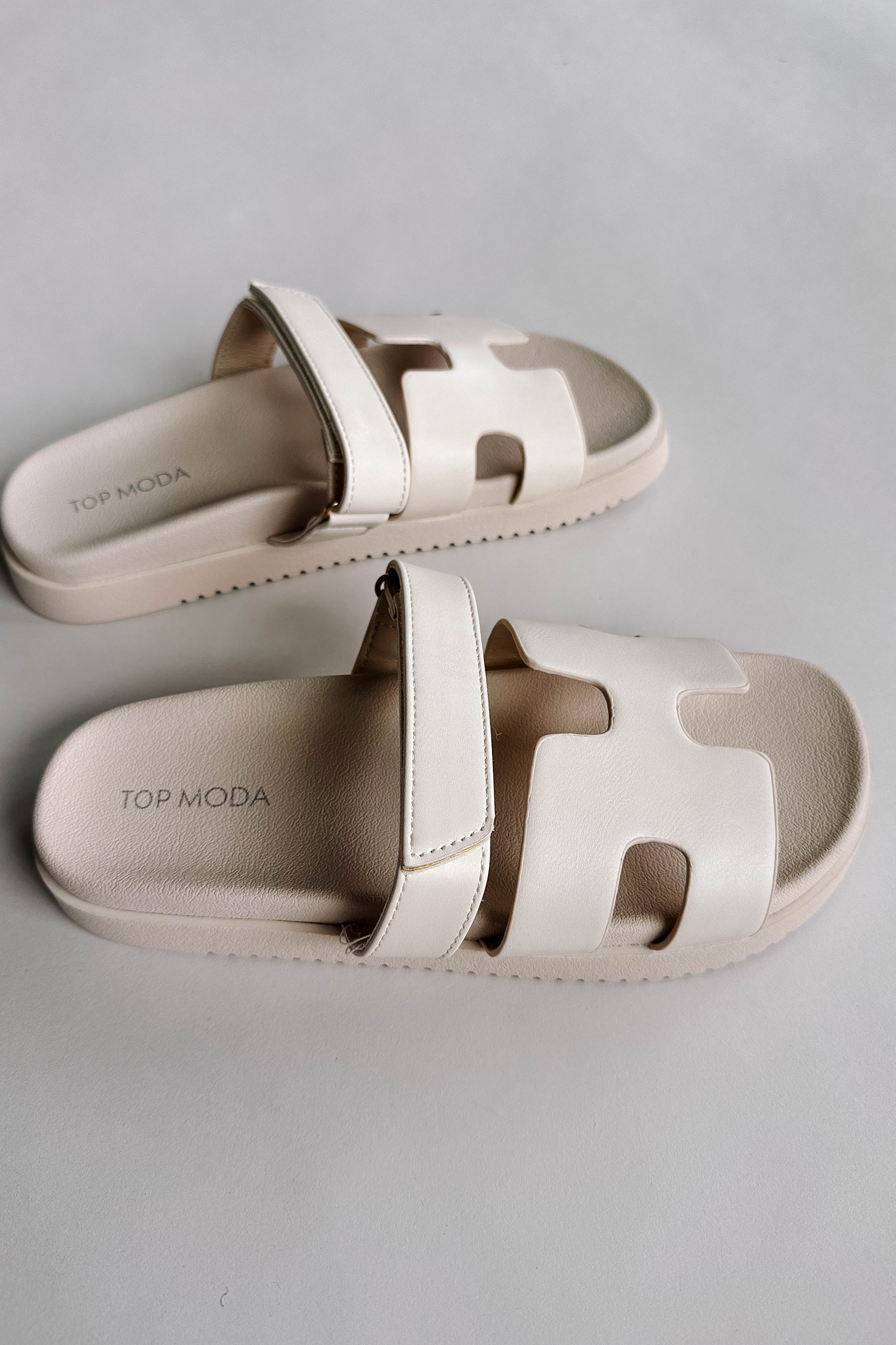 Side view of the Jade Strap Sandal in Ivory which features ivory leather fabric, slide-on style, H-shaped strap, adjustable velcro strap and round toe.