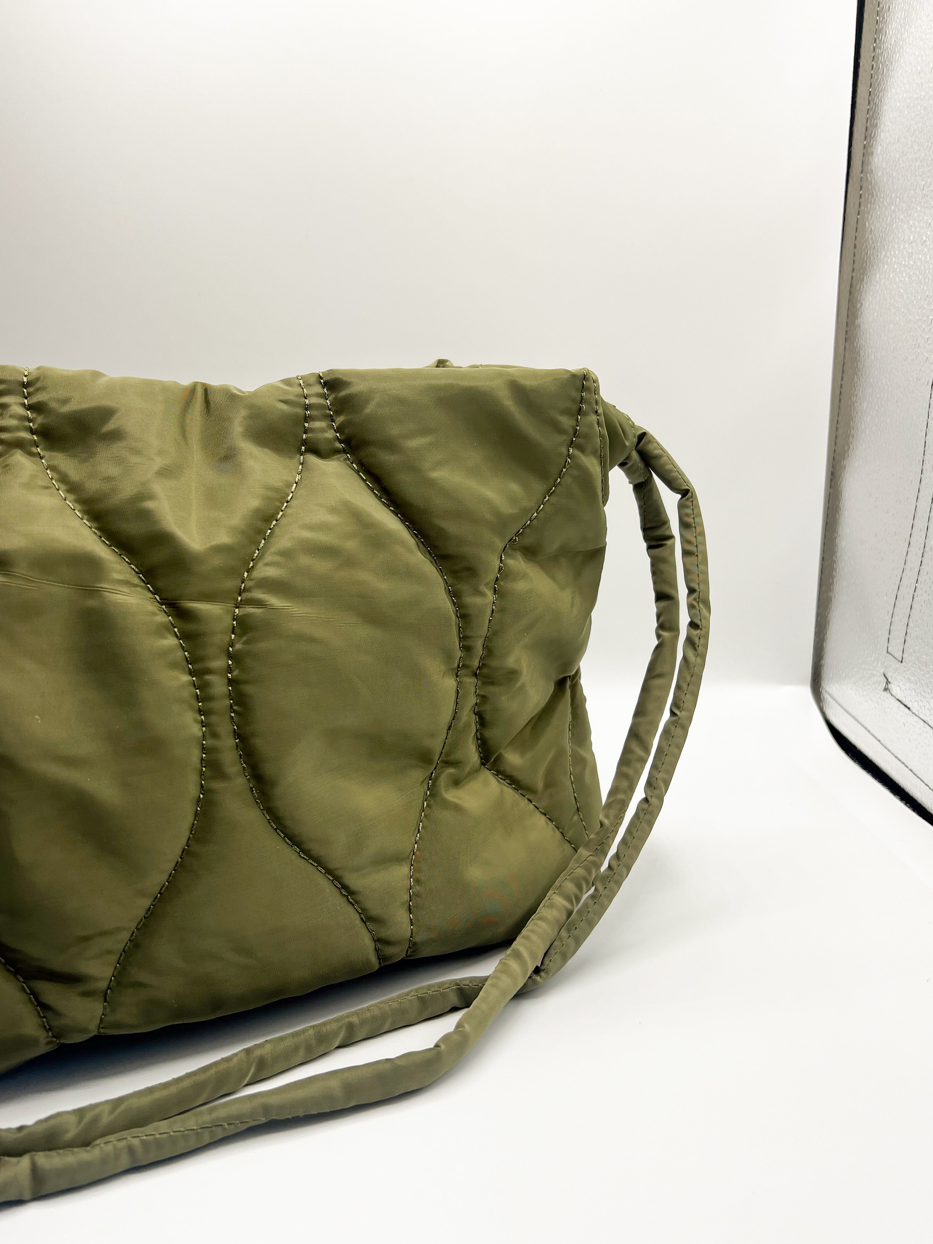 Close up of the Ryleigh Olive Green Bag. This features light olive lightweight fabric, quilted design, two skinny straps, button snap closure and light sage lining with pockets.