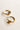 Close up side image of the Ava Gold Knot Hoop Earrings that feature small gold hoops with a knot design and clasp closure, shown on cream paper..