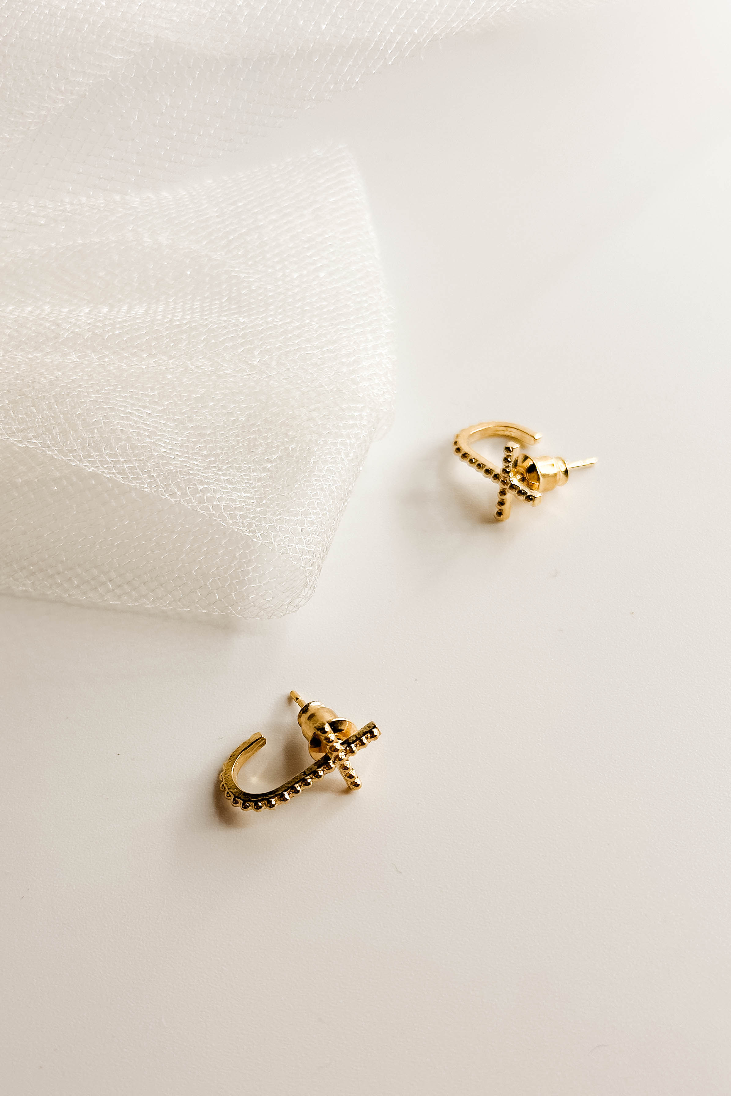 Close up detailed view of the Grace Gold Cross Stud Earring which features mini gold, open cross shaped huggies with hobnail design.