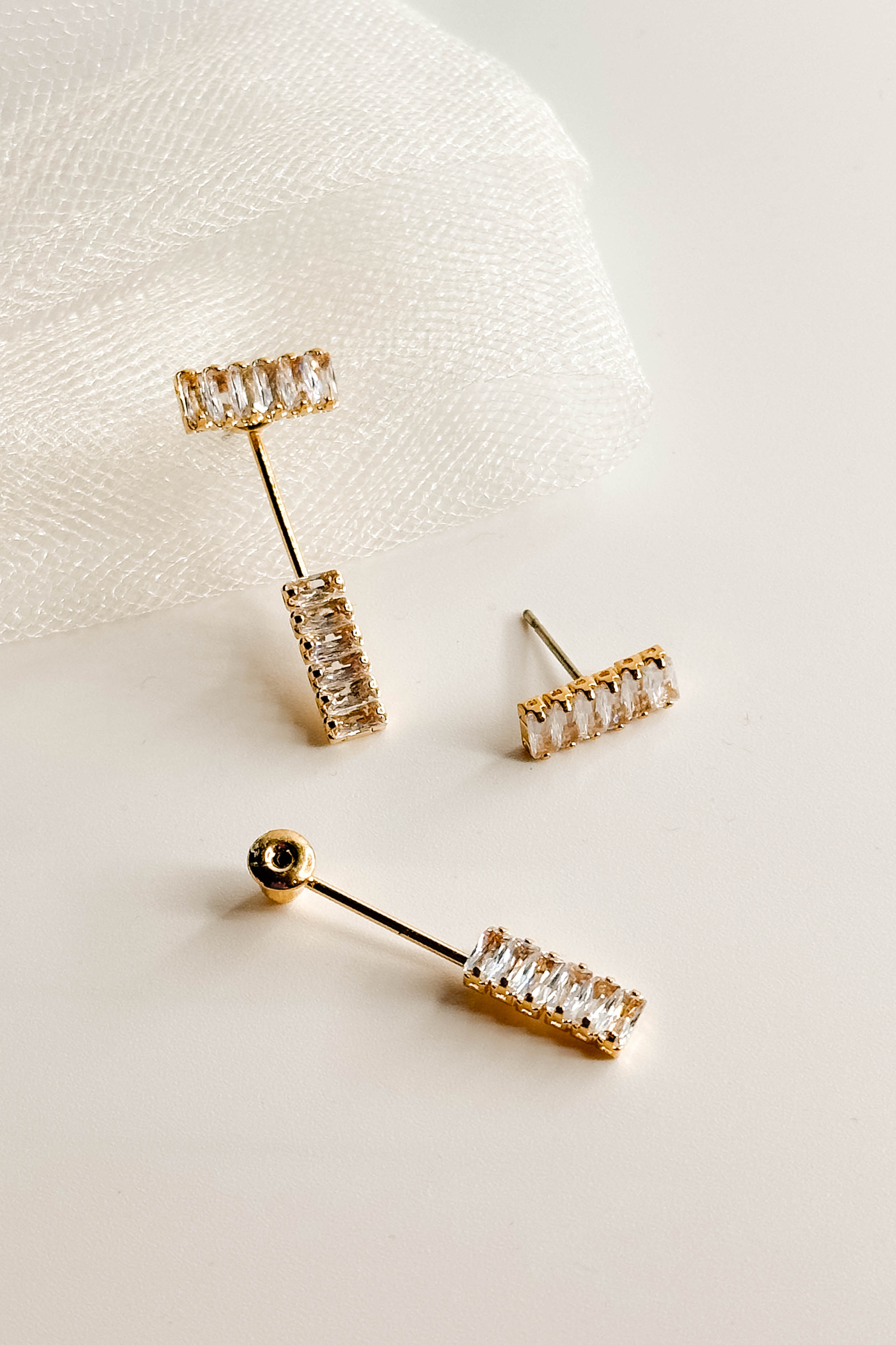Top view of the So Easy Earrings which features cluster of clear stones linked by a gold bar with another set of clear stones, shown on white paper.