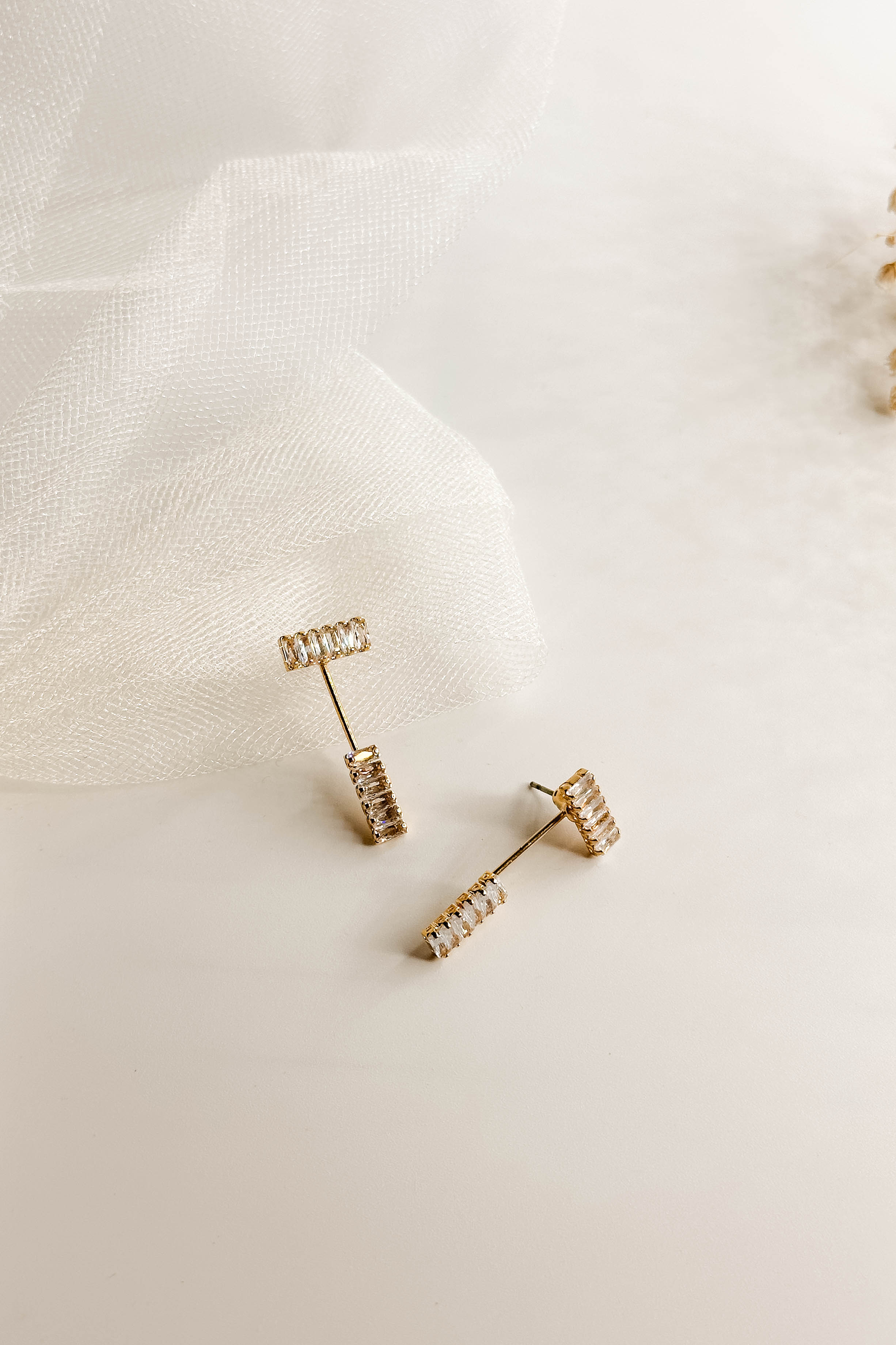Top view of the So Easy Earrings which features cluster of clear stones linked by a gold bar with another set of clear stones, shown on white paper.