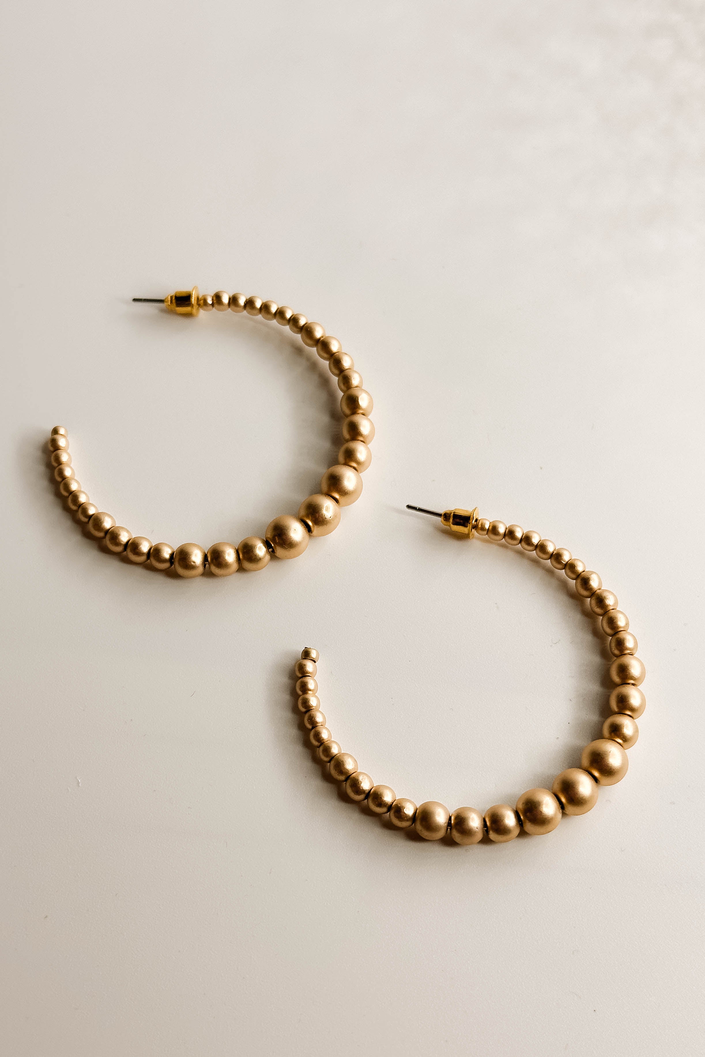 Close up flat lay of the Angela Gold Beads Open Hoop which features open medium gold beaded hoops.