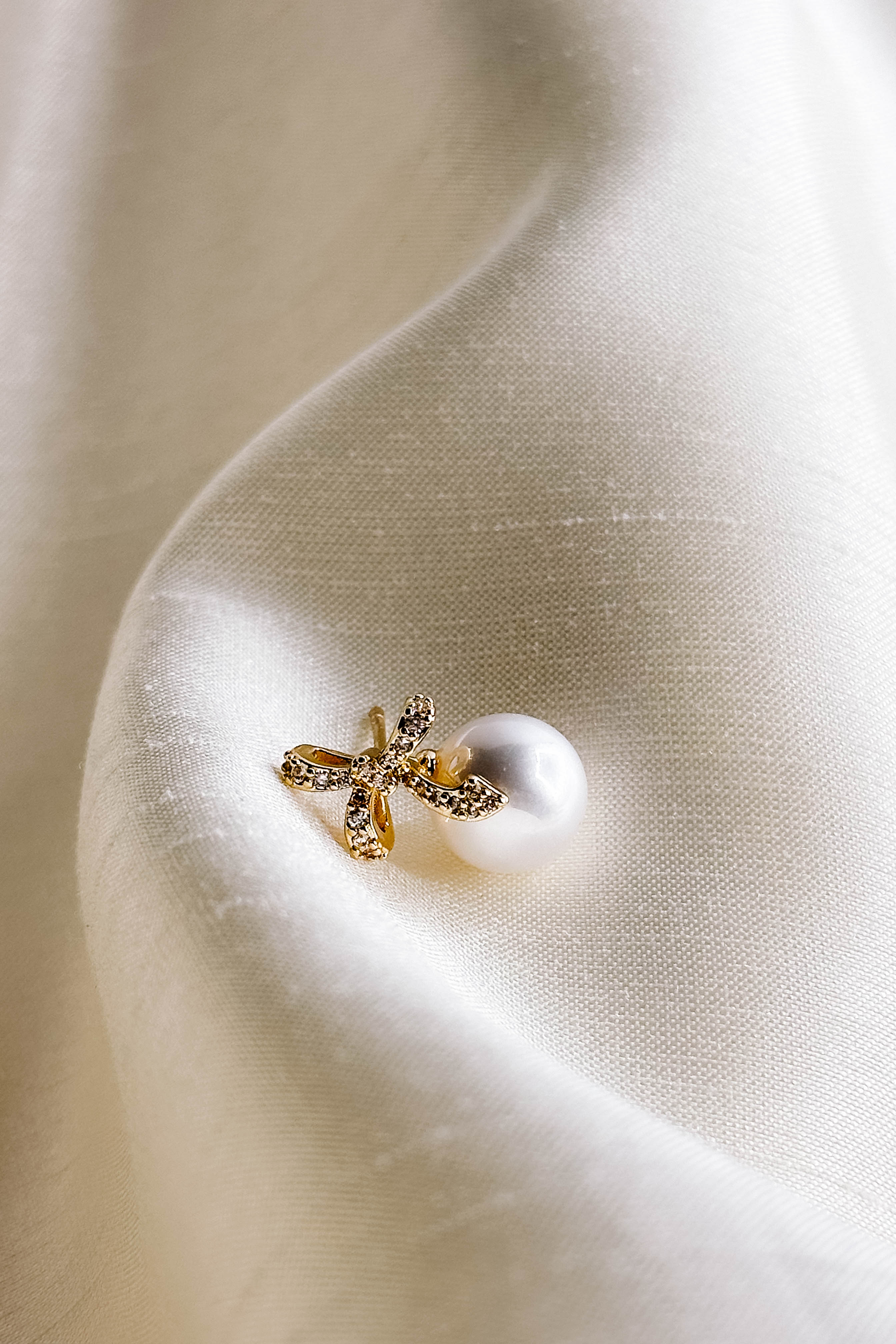 Flat lay close up view of pearl earring with gold and rhinestone bow