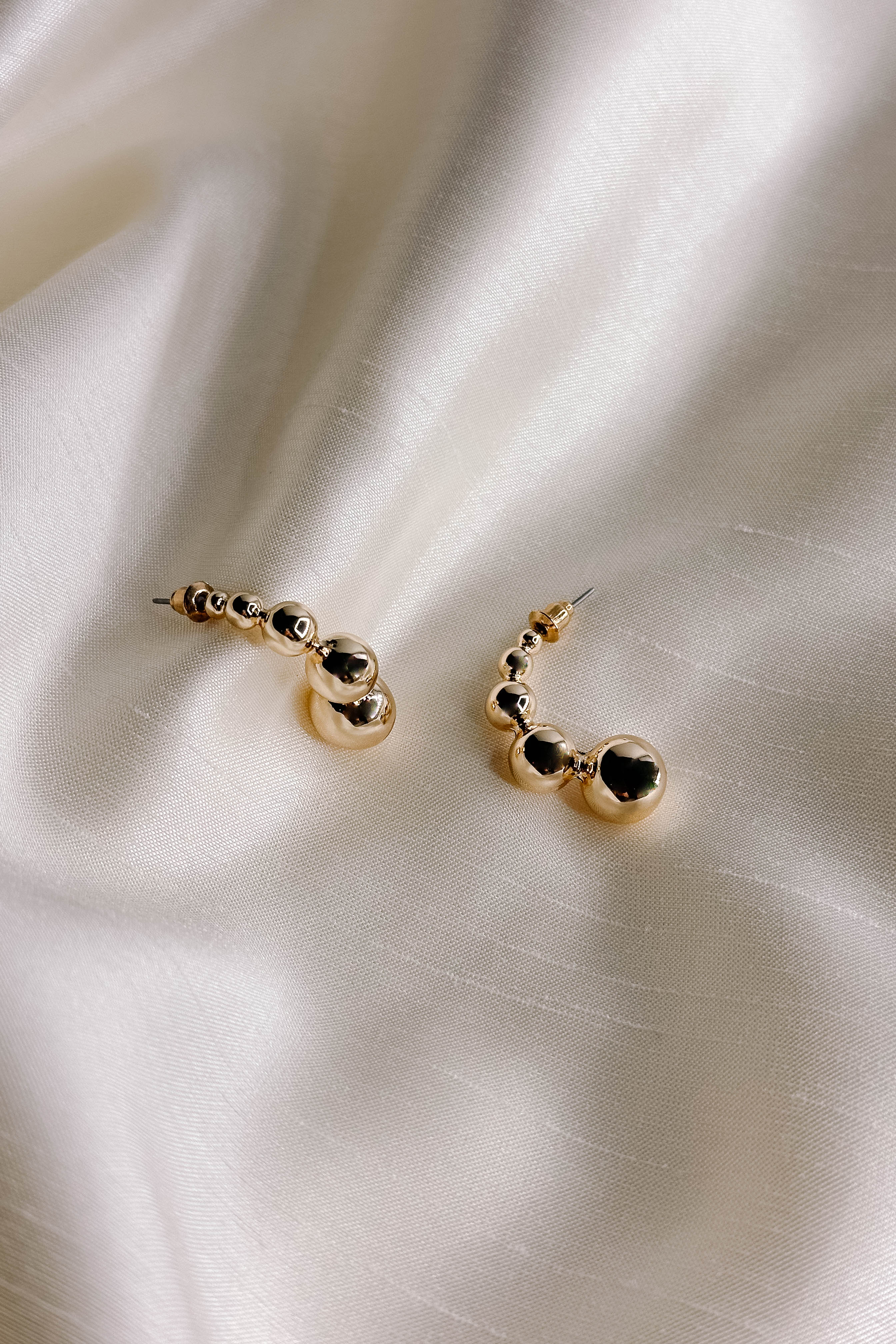 Flat lay detailed view of the Aurora Gold Bead Scooped Earring which features open hoops with small, medium and large gold beads.
