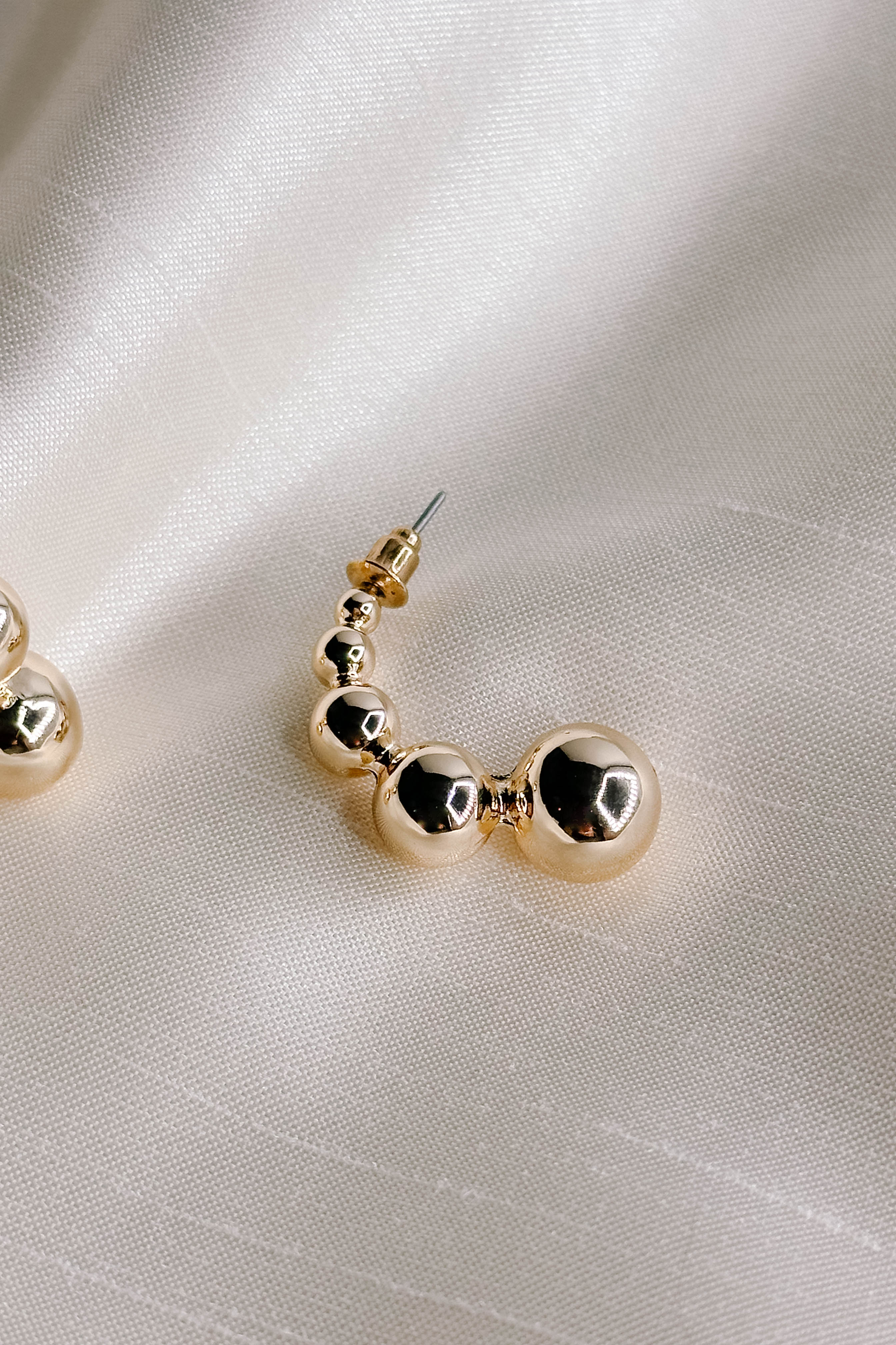 Flat lay detailed view of one of the Aurora Gold Bead Scooped Earring which features open hoops with small, medium and large gold beads.