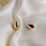 Top view flat lay of the Claire Gold Teardrop Stud Earrings that have thick gold scooped studs, shown on cream fabric..