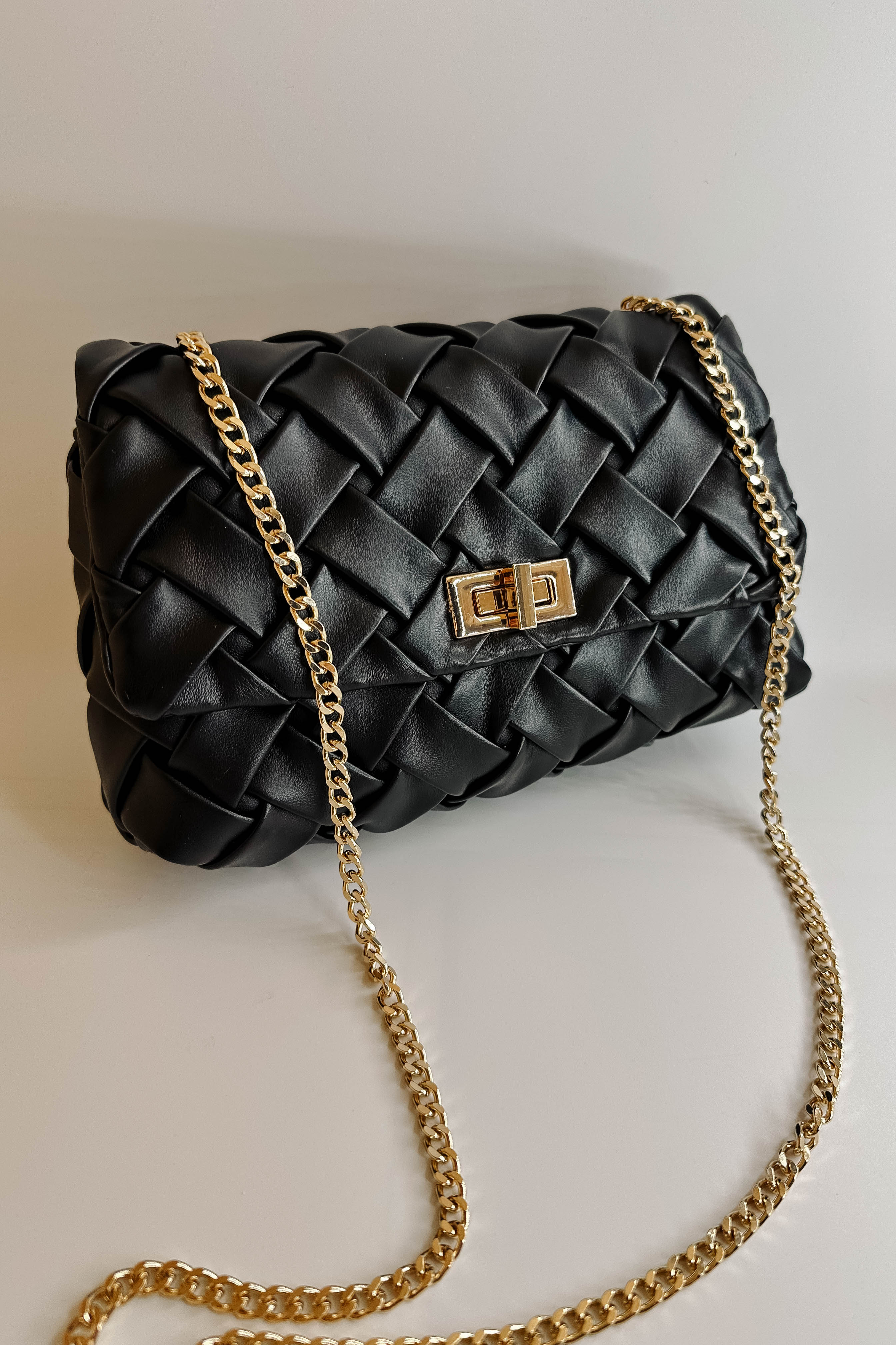 Front view of the Carrie Black Leather Woven Purse which features black woven leather fabric, gold button closure and gold chain link strap.