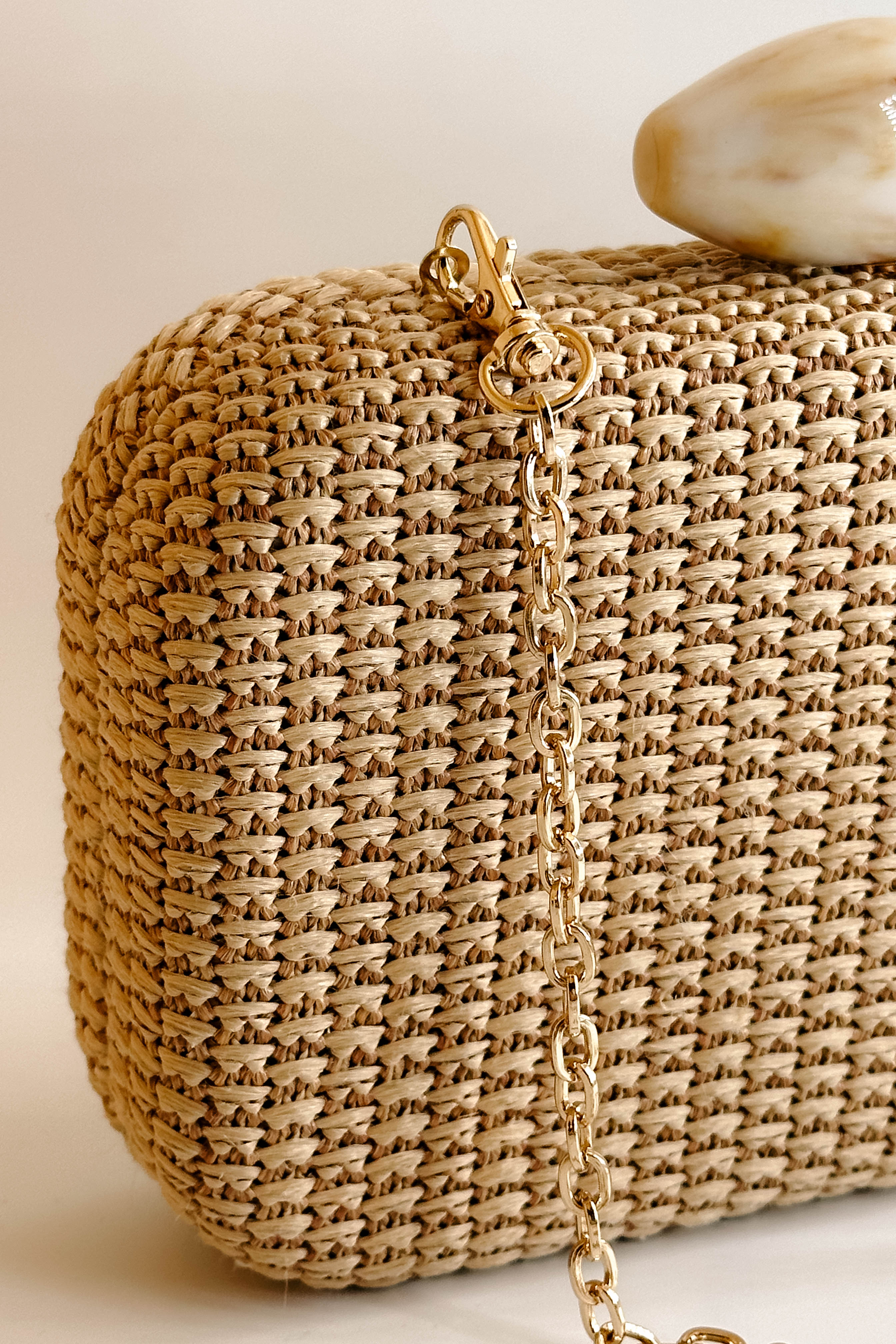 Detailed view of the chain on the Frankie Clutch. It features a woven natural texture with an oval pearl closure. On the inside, is a gold chain attachment to be transformed as a crossbody.