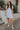 Full body view of female model wearing the The Ella Light Blue Eyelet Mini Dress which features light blue cotton fabric with an eyelet floral pattern, mini length, light blue lining, a sweetheart neckline, short puff sleeves with tie details, and a smocked back.