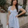 zfront view of female model wearing the The Ella Light Blue Eyelet Mini Dress which features light blue cotton fabric with an eyelet floral pattern, mini length, light blue lining, a sweetheart neckline, short puff sleeves with tie details, and a smocked back.