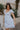 side view of female model wearing the The Ella Light Blue Eyelet Mini Dress which features light blue cotton fabric with an eyelet floral pattern, mini length, light blue lining, a sweetheart neckline, short puff sleeves with tie details, and a smocked back.