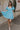 Full body view of female model wearing the Gloria Light Blue Short Sleeve Mini Dress which features aqua blue cotton fabric, aqua blue lining, mini length, ruffle tiered details, a sweetheart neckline with drawstring ties, a smocked back, and short puff sleeves.