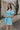 Side view of female model wearing the Gloria Light Blue Short Sleeve Mini Dress which features aqua blue cotton fabric, aqua blue lining, mini length, ruffle tiered details, a sweetheart neckline with drawstring ties, a smocked back, and short puff sleeves.