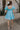 Full body  back view of female model wearing the Gloria Light Blue Short Sleeve Mini Dress which features aqua blue cotton fabric, aqua blue lining, mini length, ruffle tiered details, a sweetheart neckline with drawstring ties, a smocked back, and short puff sleeves.