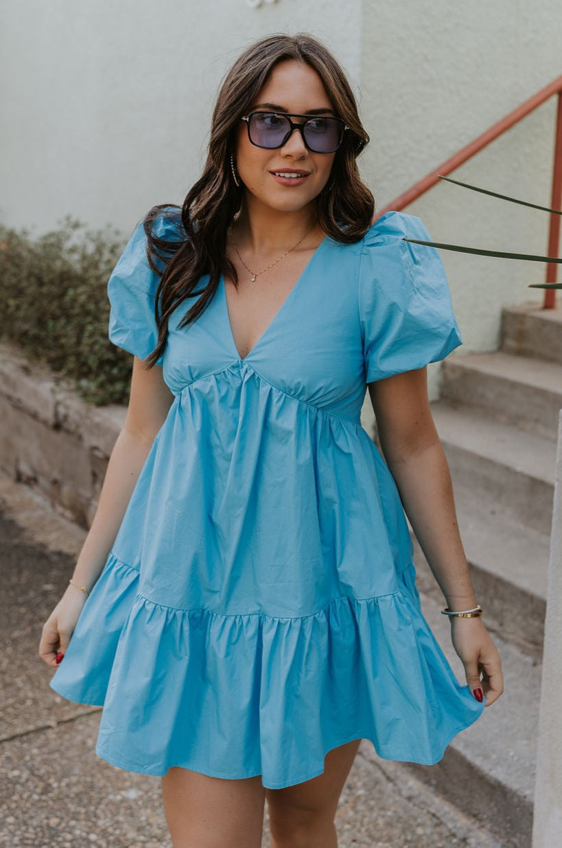 Front view of female model wearing the Stephanie Light Blue Short Puff Sleeve Mini Dress which features light blue light weight fabric, mini length, flared skirt, plunge neckline, short puff sleeves, tie closure in the back and monochrome side zipper with hook closure.