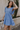 Side view of model wearing the Nicole Blue Ruffle Short Sleeve Mini Dress which features chambray blue light weight fabric, mini length, chambray blue lining, two-tiered design, two side pockets, square neckline and ruffle short sleeves.