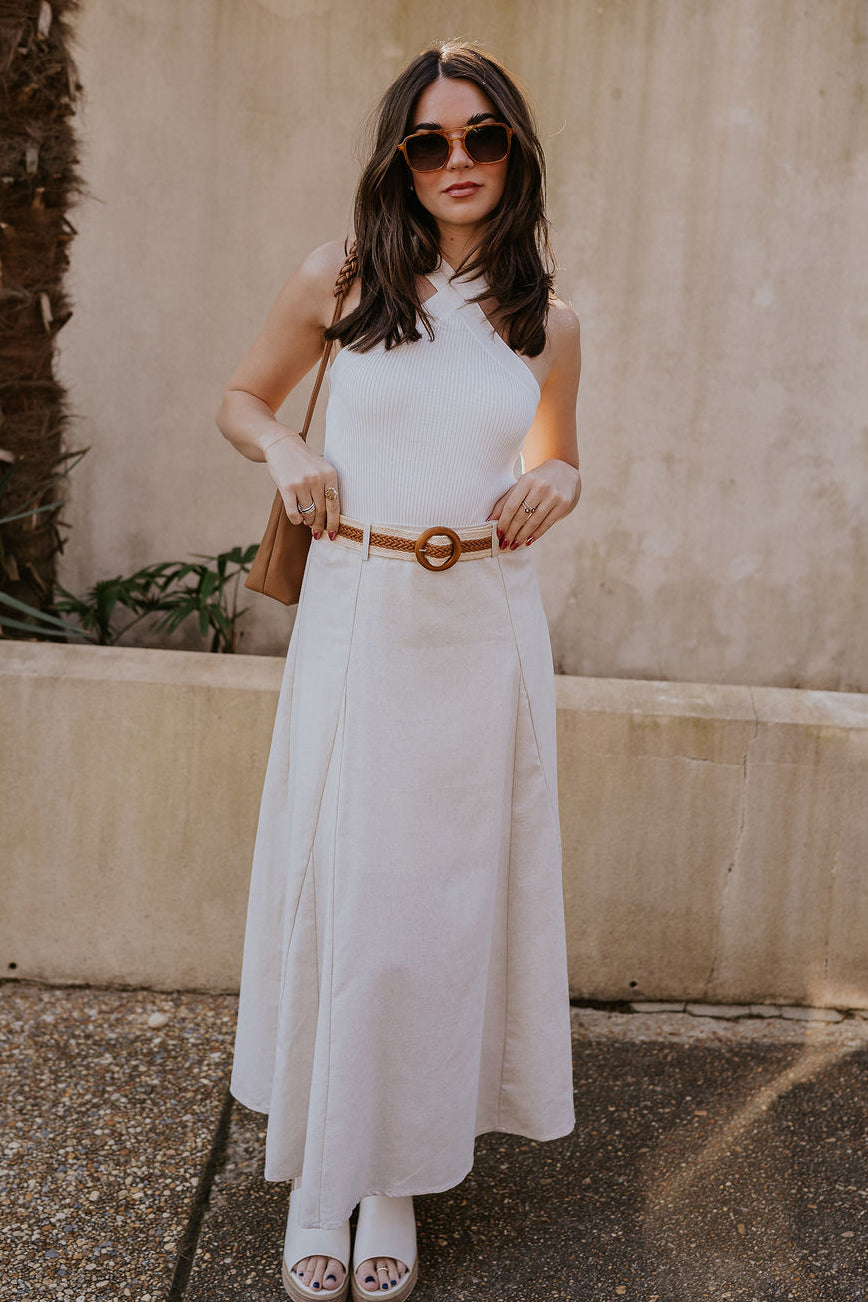 Full body view of model wearing the Seychelles Linen Midi Skirt which features natural linen fabric, midi length, flared skirt, natural lining, belt loops, brown and natural crochet adjustable belt and monochrome side zipper with hook closure.