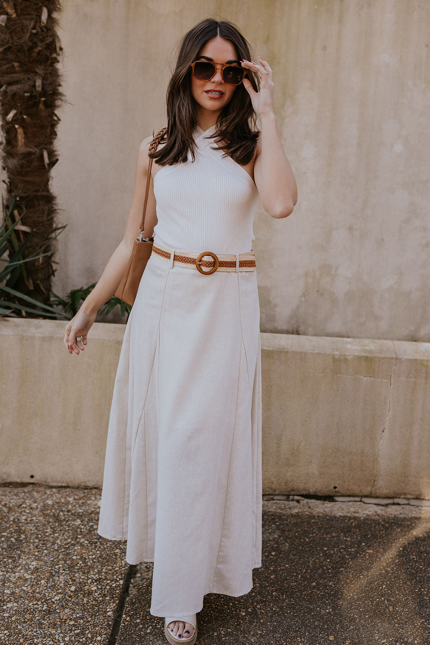 Full body view of model wearing the Seychelles Linen Midi Skirt which features natural linen fabric, midi length, flared skirt, natural lining, belt loops, brown and natural crochet adjustable belt and monochrome side zipper with hook closure.
