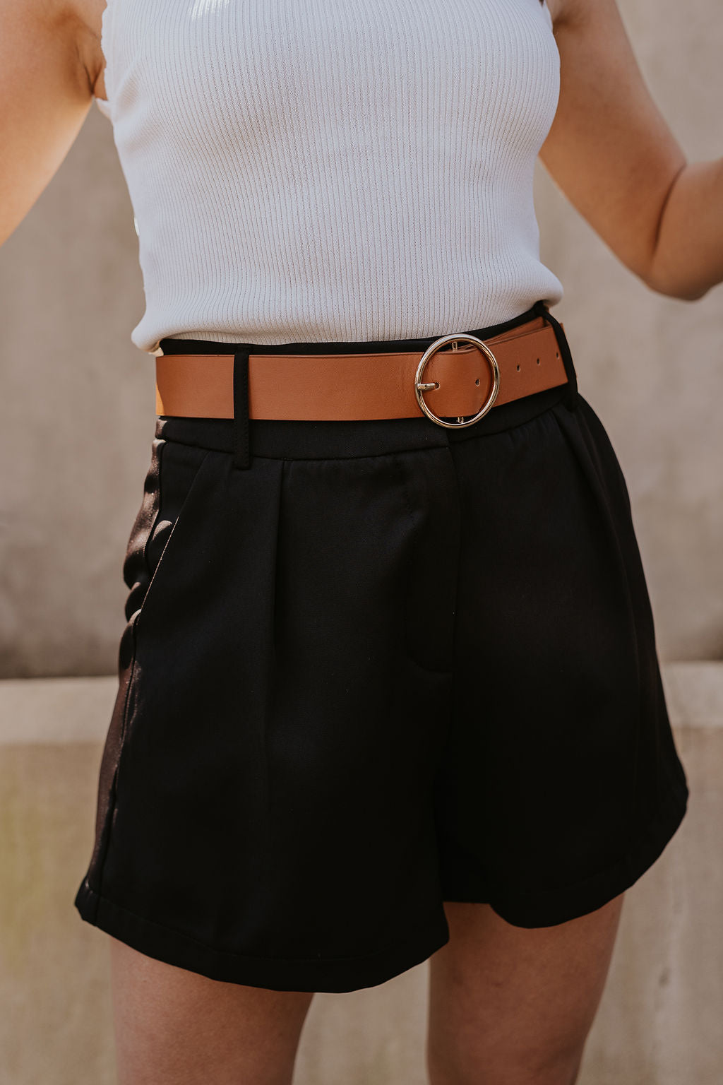 Close up view of model wearing the Tiffany Black Shorts which features black fabric with black lining, a front zipper with hook closures, side pockets, faux back pocket details, belt loops, and front pleats.