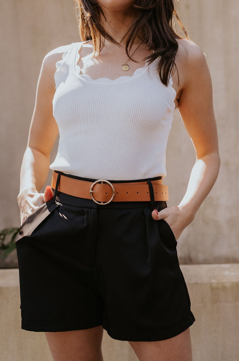 Front view of model wearing the Tiffany Black Shorts which features black fabric with black lining, a front zipper with hook closures, side pockets, faux back pocket details, belt loops, and front pleats.