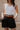 Front view of model wearing the Tiffany Black Shorts which features black fabric with black lining, a front zipper with hook closures, side pockets, faux back pocket details, belt loops, and front pleats.