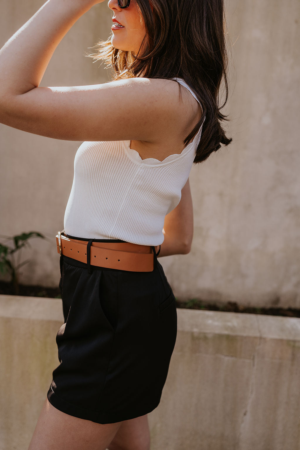 Side view of model wearing the Tiffany Black Shorts which features black fabric with black lining, a front zipper with hook closures, side pockets, faux back pocket details, belt loops, and front pleats.