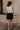 Full body back view of model wearing the Tiffany Black Shorts which features black fabric with black lining, a front zipper with hook closures, side pockets, faux back pocket details, belt loops, and front pleats.
