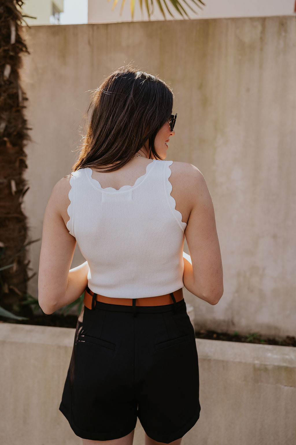 Back view of model wearing the Veronica Off White Scalloped Tank which features white ribbed fabric, scalloped trim, thick straps, and a round neckline.