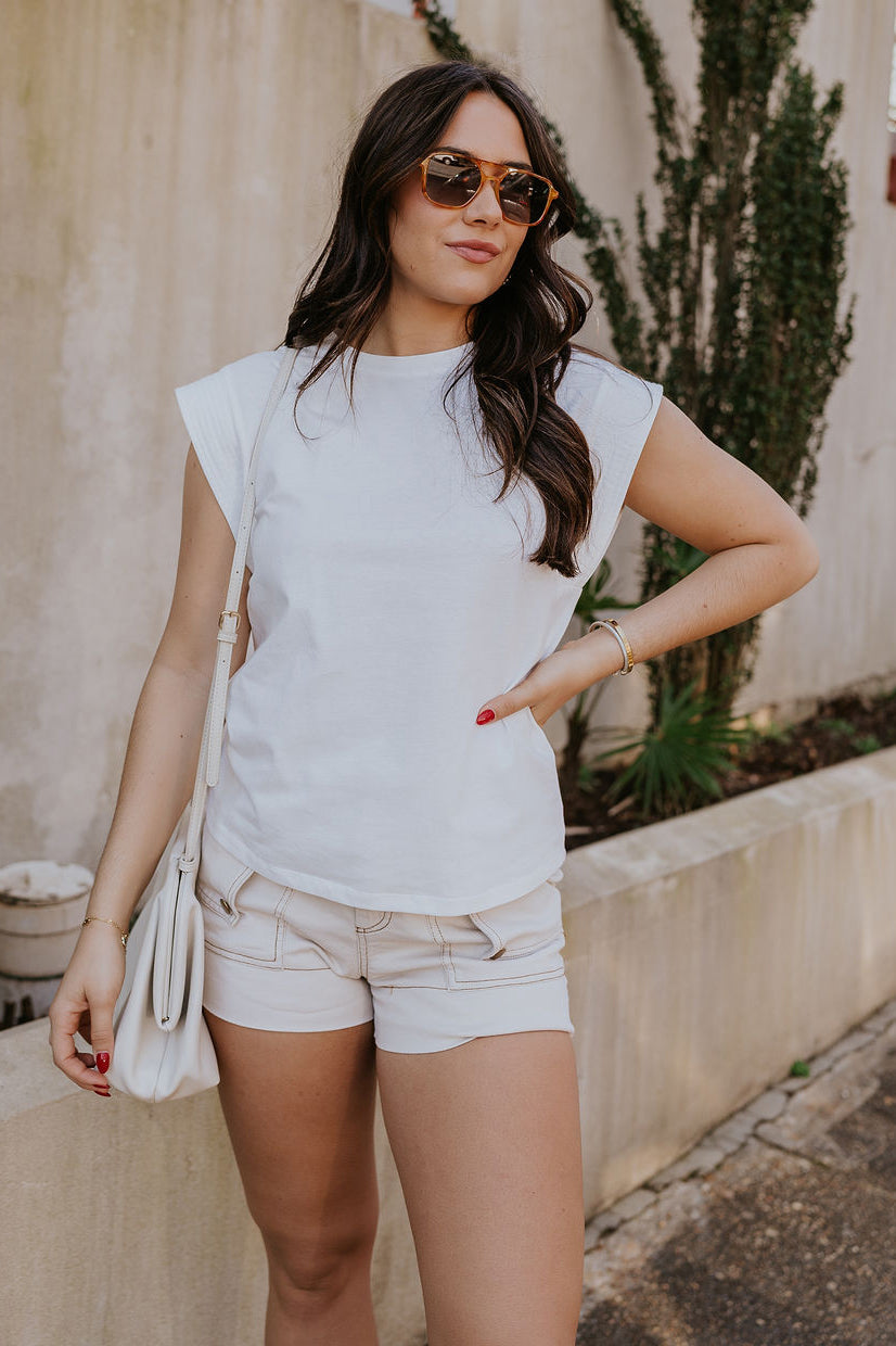 Front view of model wearing the Iris Off White Sleeveless Top which features off white cotton fabric, round neckline and short sleeves with stitched ribbed hem details.
