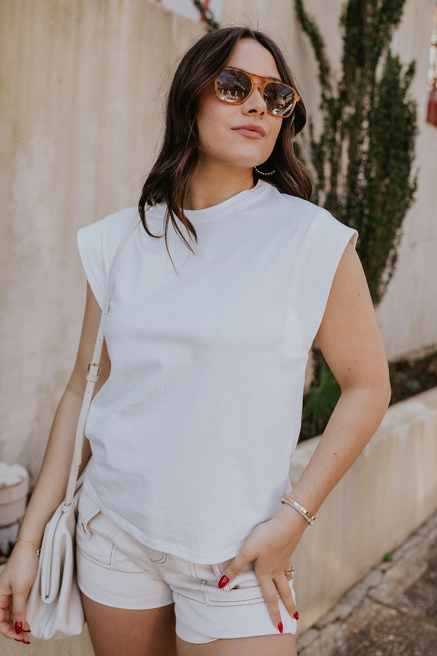 Front view of model wearing the Iris Off White Sleeveless Top which features off white cotton fabric, round neckline and short sleeves with stitched ribbed hem details.