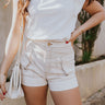 Front view of model wearing the Nova Ecru Denim Shorts which features ecru denim fabric, light brown stitch details, gold button details, two front pockets, two back pockets, front zipper with button closure and elastic back waistband.