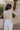 Back view of model wearing the Lyla Light Taupe Knit Tank which features light taupe open knit fabric, round neckline and sleeveless.