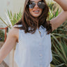 Front view of model wearing the Leah Light Denim Sleeveless Tank which features light blue tencel fabric, fray hem, white tortoise button up closure, collared neckline and sleeveless.