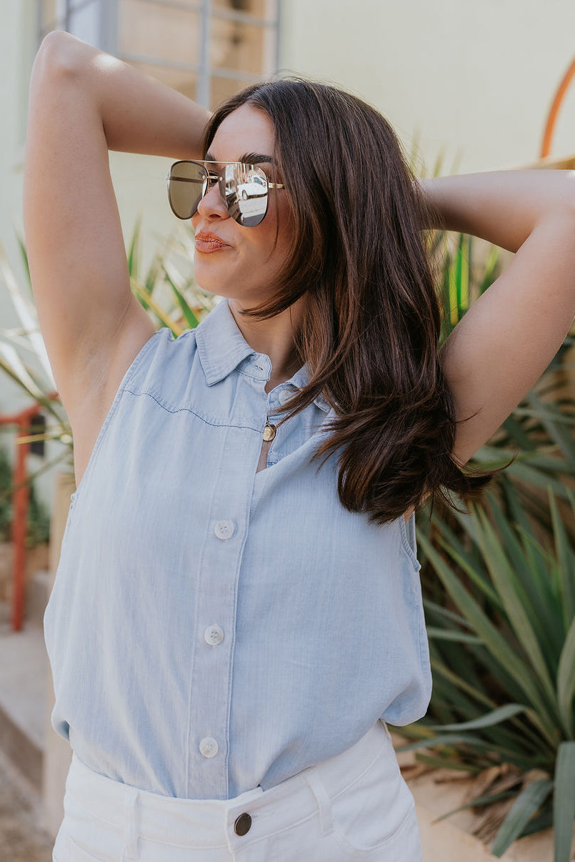 Front view of model wearing the Leah Light Denim Sleeveless Tank which features light blue tencel fabric, fray hem, white tortoise button up closure, collared neckline and sleeveless.