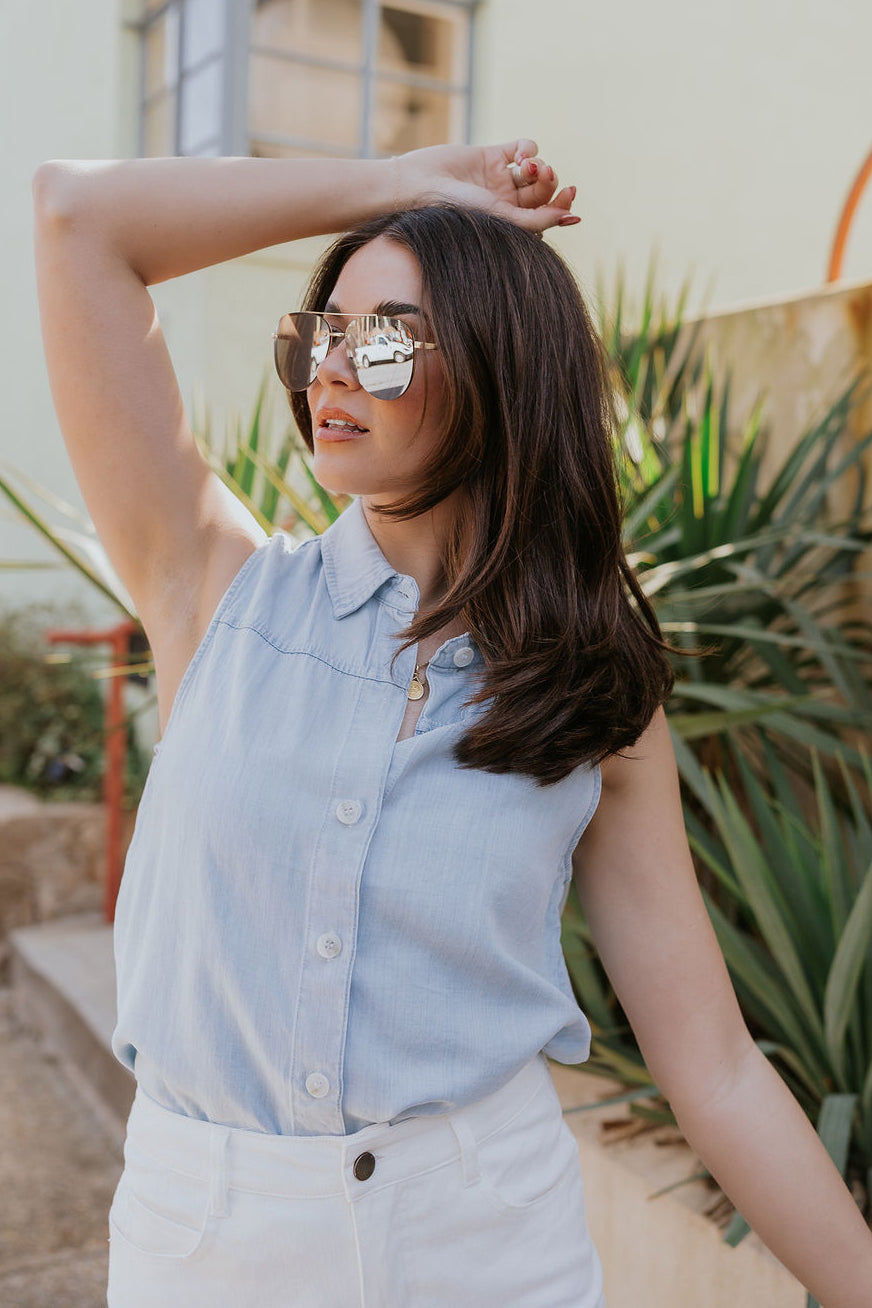 Front view of model wearing the Leah Light Denim Sleeveless Tank which features light blue tencel fabric, fray hem, white tortoise button up closure, collared neckline and sleeveless.