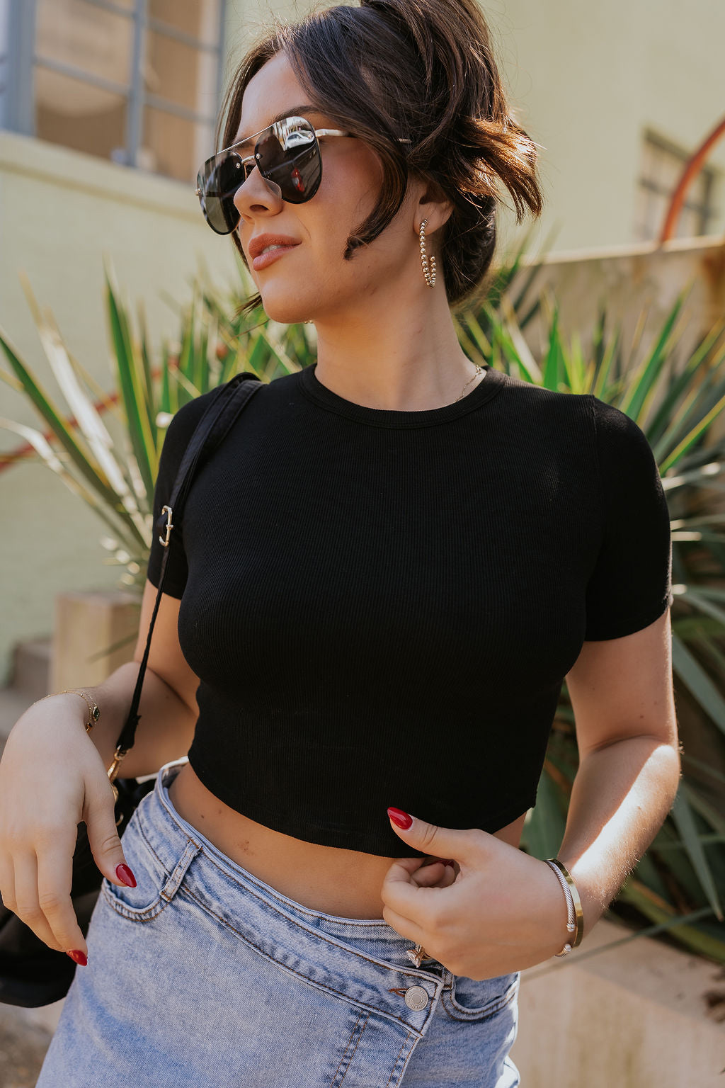 Front view of model wearing the Lucy Black Cropped Short Sleeve Top which features black ribbed knit fabric, cropped waist, round neckline and short sleeves.