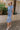 Full body side view of model wearing the Addison Washed Denim Front Tie Midi Dress which features washed denim fabric, midi length, brown tortoise button up front closure, front cinch tie waist, collared neckline and short sleeves.