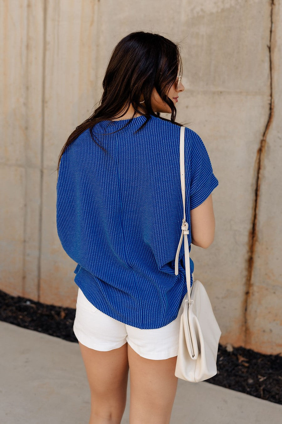 Back view of model wearing the Everly Blue Ribbed Short Sleeve Top that features dark blue and light blue contrast ribbing, a round neckline, and short dolman sleeves with ribbed cuff details.