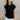 Front view of model wearing the Iris Black Sleeveless Top that features black cotton fabric, a round neckline, and short sleeves with stitched ribbed hem details.