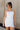 Front view of model wearing the Brielle White Sleeveless Mini Dress that features white stretchy fabric, mini length, white lining, a layered skirt, pleated cinched side detail, a square neckline, adjustable straps, and monochrome back zipper with a hook closure.