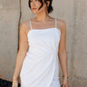 Front view of model wearing the Brielle White Sleeveless Mini Dress that features white stretchy fabric, mini length, white lining, a layered skirt, pleated cinched side detail, a square neckline, adjustable straps, and monochrome back zipper with a hook closure.