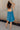 Full body back view of model wearing the Lucille Dark Turquoise Sleeveless Mini Dress which features dark turquoise fabric, a smocked sweatheart neckline and back, smocked thick straps, and dark turquoise lining.