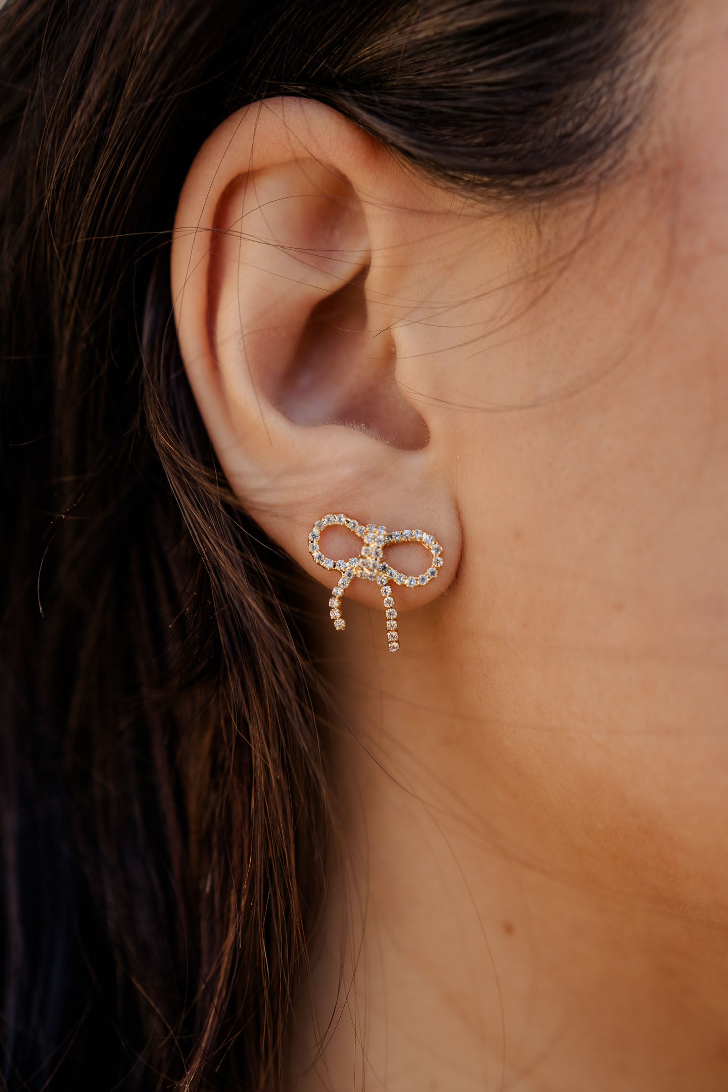 model wearing gold bow stud earrings with clear rhinestones in ear