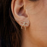 model wearing gold bow stud earrings with clear rhinestones in ear