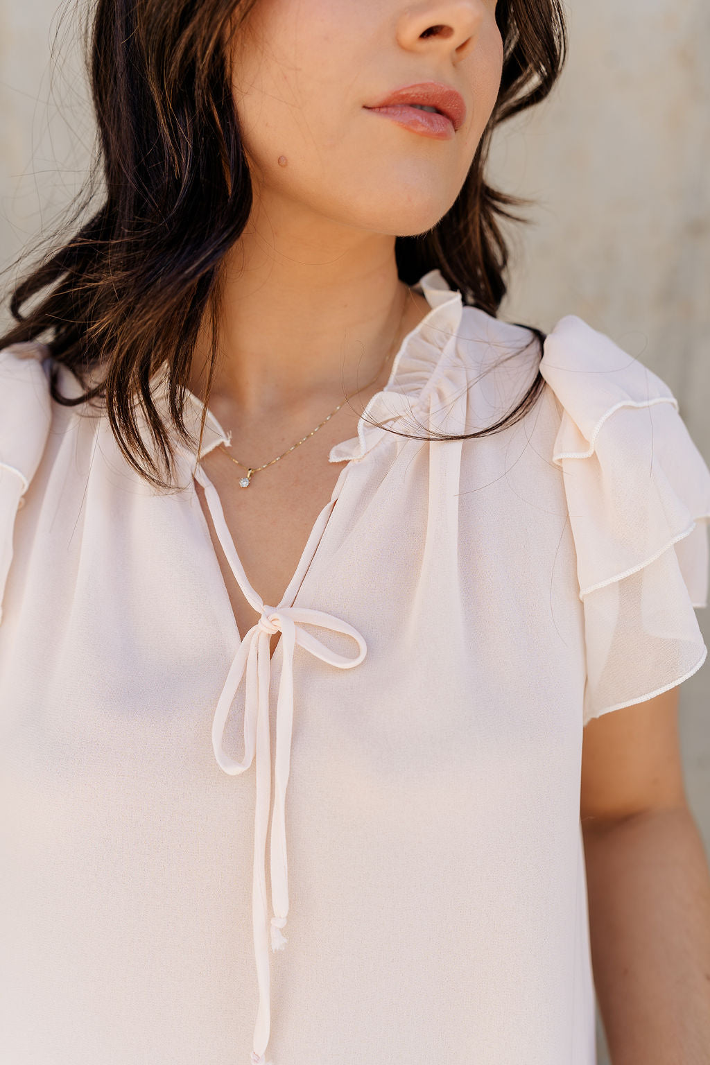 Close up view of model wearing the Olivia Cream Ruffle Short Sleeve Top which features cream sheer fabic, cream lining, ruffle neckline with drawstring ties, and ruffle tiered short sleeves.