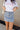 Front view of model wearing the Sloane Light Denim Wash Skirt which features light wash stretchy denim fabric, a front zipper with a snap closure, large side pockets with snap closures, back pockets, belt loops, and contrast stitching.