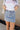 Front view of model wearing the Sloane Light Denim Wash Skirt which features light wash stretchy denim fabric, a front zipper with a snap closure, large side pockets with snap closures, back pockets, belt loops, and contrast stitching.