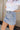 Side view of model wearing the Sloane Light Denim Wash Skirt which features light wash stretchy denim fabric, a front zipper with a snap closure, large side pockets with snap closures, back pockets, belt loops, and contrast stitching.