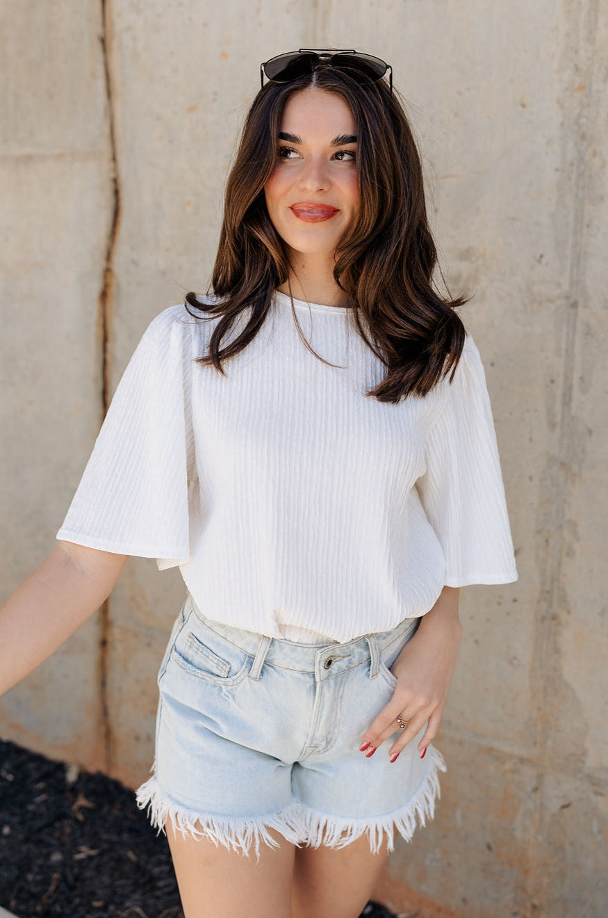 Front view of model wearing the Merritt Ivory Short Sleeve Top which features ivory textured fabric, round neckline, short sleeves and back key hole with monochrome button closure.